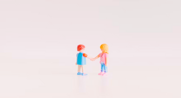 Two Lego figurines stand facing each other, holding hands in agreement